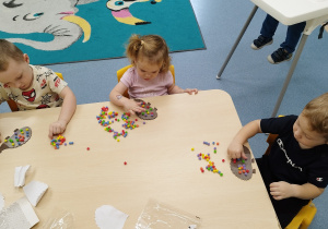 dzieci siedzą przy stole i przyklejają kolorowe kulki jeżykom