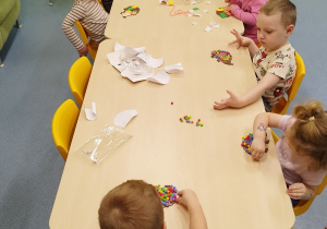 dzieci siedzą przy stoliku i wykonują pracę plastyczną