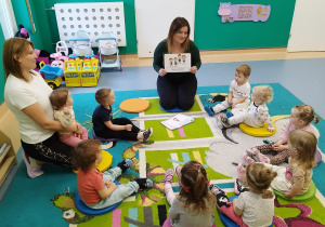 opiekunki siedząz dziećmi na dywanie, opiekunka pokazuje ilustrację