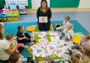 opiekunka pokazuje ilustracje dzieciom siedzącym na dywanie