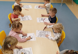dzieci siedzą przy stoliku i kolorują kredkami
