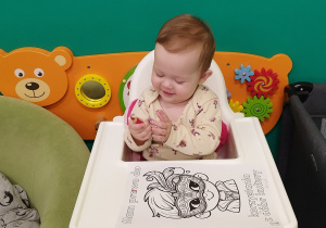 dziecko siedzi w krzesełku, trzyma kredkę