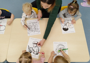 dziei kolorują kredkami obrazki, opiekunka im pomaga