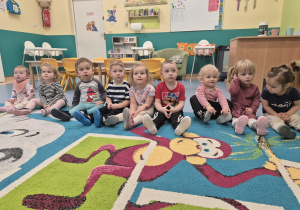 dzieci siedzą w jednej linii na dywanie