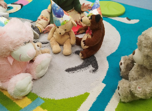 na dywanie siedzą pluszowe misie w urodzinowych czapeczkach