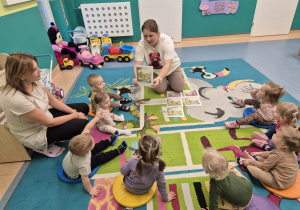 opiekunka pokazuje dzieciom siedzącym na dywanie ilustrację z opowiadania o misiu