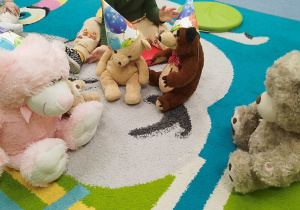 na dywanie siedzą pluszowe misie w urodzinowych czapkach