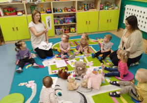 dzieci i opiekunki siedzą na dywanie , opiekunka pokazuje obrazek misia