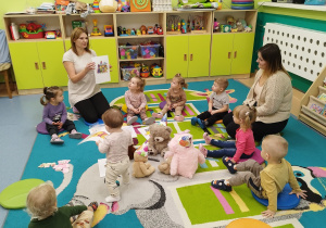dzieci i opiekunki siedzą na dywanie, opiekunka pokazuje obrazek misia