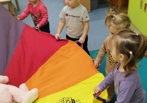 dzieci trzymają chustę, na której leżą misie