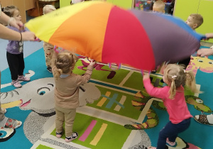 dzieci podrzucają misie leżące na kolorowej chuście