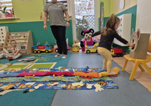 dziewczynka wkłada rękę z rybą do pyszczka misia, opiekunka patrzy