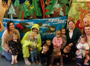 dzieci z opiekunkami i aktorem w przebraniu żaby pozują do zdjęcia na bajkowym tle