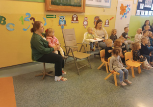 dzieci i opiekunki siedzą na krzesłach