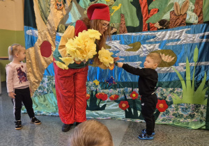 dwoje dzieci zbiera kwiaty z podłogi i podaje aktorce-krasnalowi