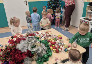 dzieci wraz z opiekunką wieszają bombki na choince
