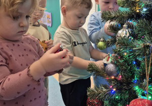 dzieci wieszają bombki na gałązkach choinki