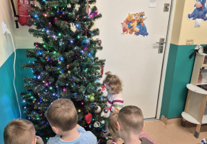 dzieci stoją wokół choinki, wieszają bombki