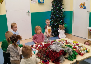 dzieci podchodzą do stołu, na którym leżą ozdoby choinkowe