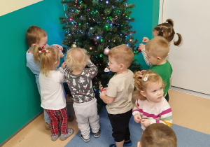 dzieci stoją wokół choinki, wieszają ozdoby