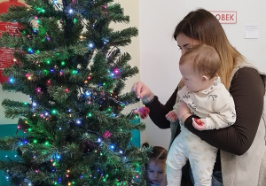 dzieci stoją wokół choinki, opiekunka trzyma na rękach dziecko