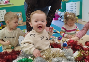 dziecko siedzi , a wokół łańcuchy choinkowe, uśmiecha się