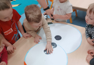 dzieci stoją wokół stolika, na którym leży bałwan, chłopiec przykleja mu guzik