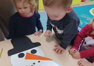 dzieci patrzą, na stoliku leży bałwan, ma oczy, kapelusz, nos