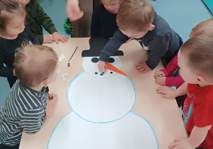 chłopiec wykleja buźkę bałwankowi