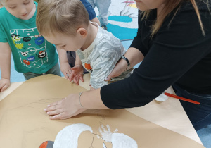 chłopiec kładzie rękę na plakacie, opiekunka pomaga