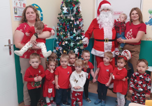 dzieci wraz z opiekunkami pozują do zdjęcia z mikołajem
