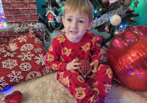 chłopiec siedzi , trzyma bombkę i uśmiecha się