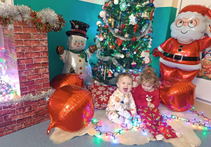 dziewczynki siedzą , w tle choinka, dmuchany mikołaj i bałwan