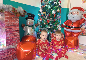 chłopcy siedzą, w tle choinka , dmuchany mikołaj i bałwan, i bombki