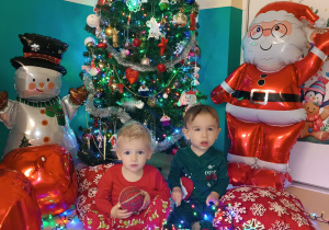 chłopcy siedzą , w tle choinka, dmuchany mikołaj, bombki i bałwan