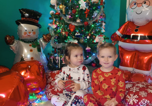 dziewczynki siedzą, jedna trzyma bombkę, druga się uśmiecha