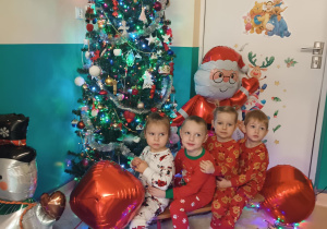 chłopcy i dziewczynki siedzą na sankach, w tle choinka