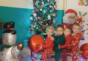 chłopcy siedzą na sankach, w tle choinka