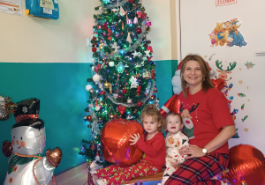 opiekunka z dzieczynkami siedzi na sankach, w tle choinka