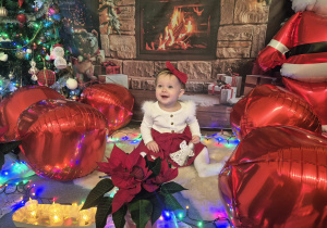 dziewczynka siedzi, uśmiecha się, wokół dużo dmuchanych bombek