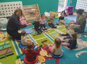 opiekunki i dzieci siedzą na dywanie i grają na instrumentach