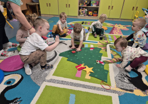 opiekunka rozdaje dzieciom ozdoby, które to one przyczepiają do choinki