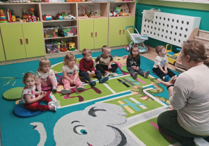 dzieci siedzą na dywanie , słuchają opowiadania opiekunki