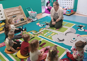 dzieci siedzą na dywanie słuchają opowiadania opiekunki