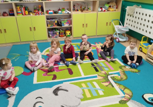 dzieci siedzą na dywanie i jedzą pierniczki