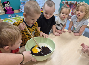 chłopiec miesza łyżką w misce, inne dzieci patrzą