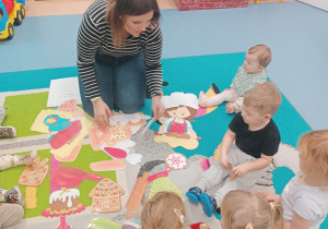 dzieci i opiekunka siedzą na dywanie i układają rozsypankę obrazkową