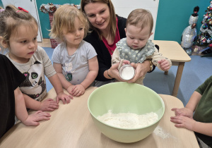 opiekunka pomaga dziewczynce wsypać do miski cukier