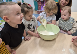 dziewczynka dodaje śmietanę do miski , a reszta dzieci patrzy