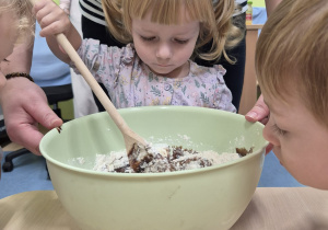 dziewczynka trzyma dużą łyżkę i miesza w misce